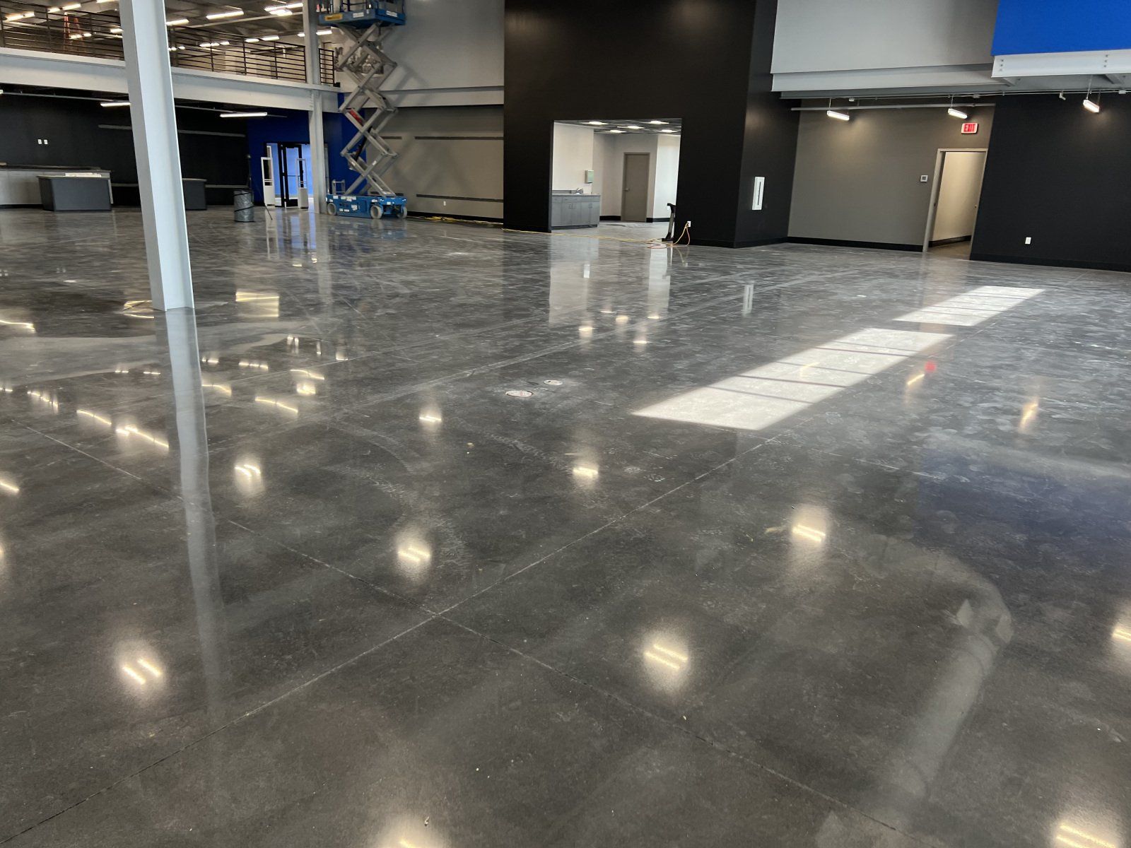 A wide, polished gray concrete floor in an open, modern interior space with black walls and overhead lighting.