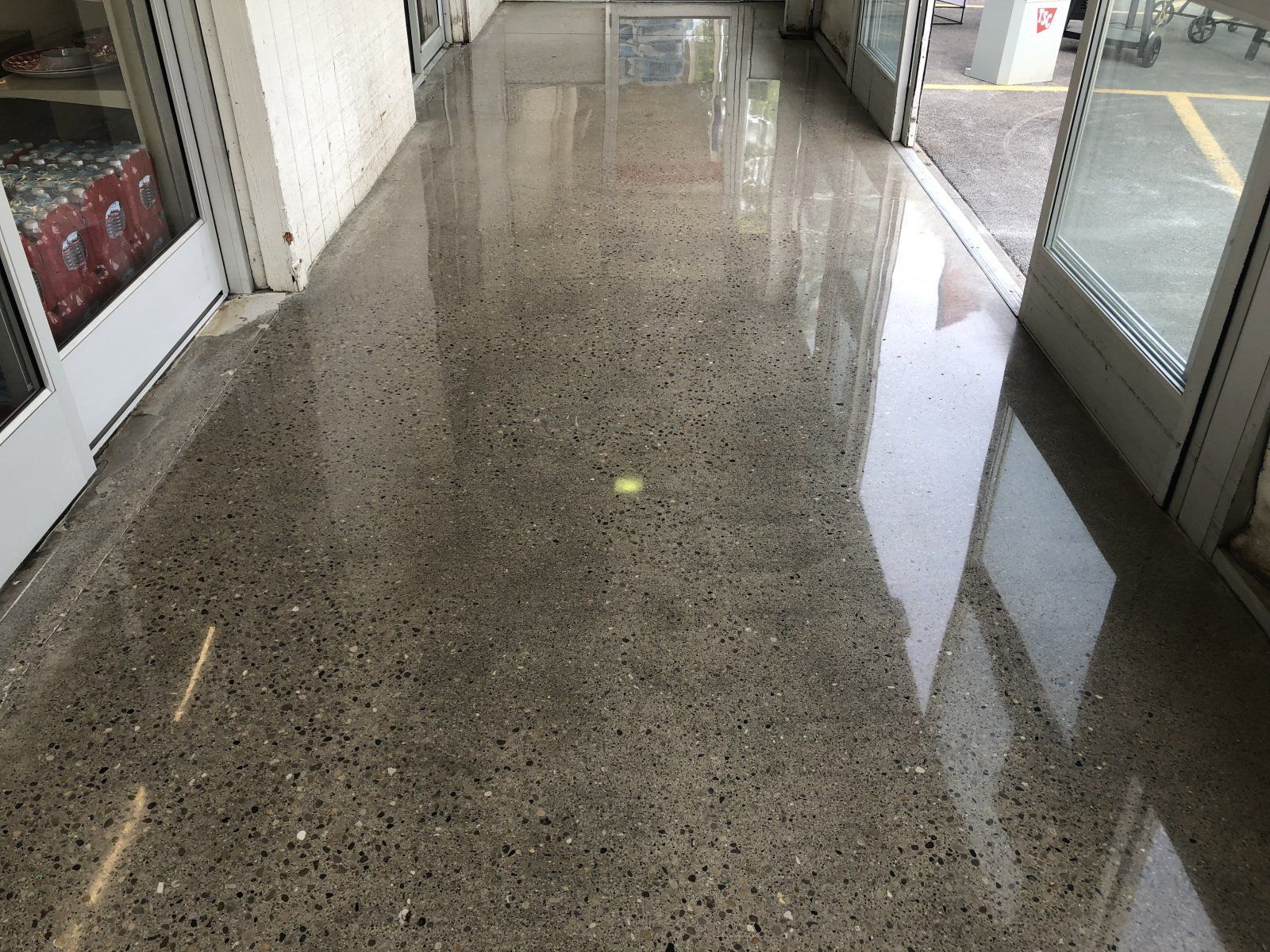 A person in a mask and work overalls operates a floor sander in an empty room with white walls.