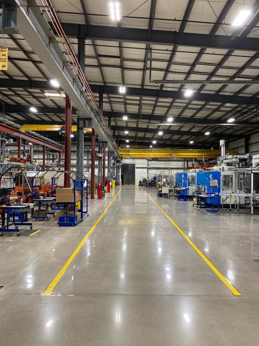 A brightly lit industrial factory floor with blue machinery on the right and yellow safety lines marking a central walkway.
