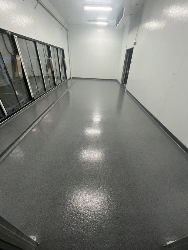 A long, narrow room with a glossy gray flecked epoxy floor, white walls, and a row of glass freezer doors.
