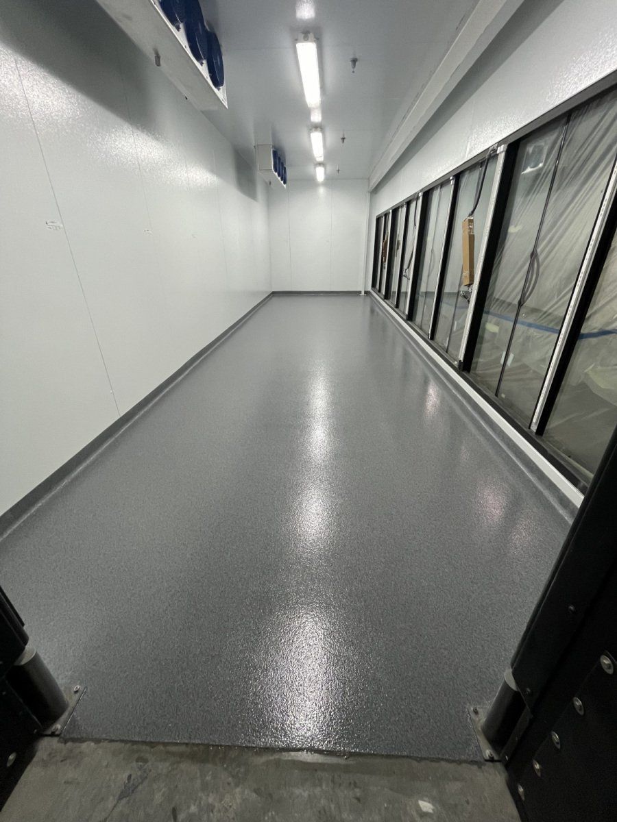 A view down a brightly lit hallway with a gray, speckled epoxy floor and glass freezer doors on the right.