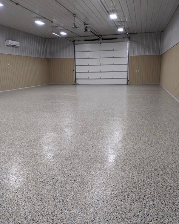 Empty garage with speckled epoxy floor, beige walls, and a closed white roll-up door.