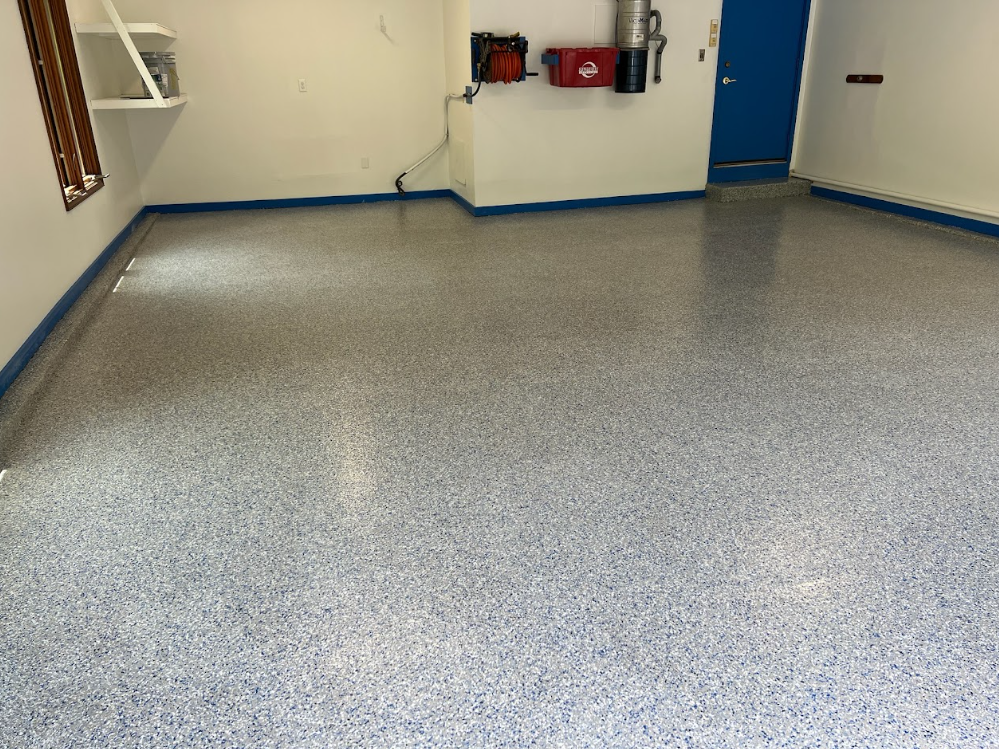 Empty speckled garage floor in a room with beige walls and a blue door.