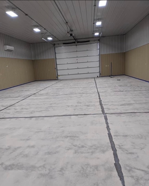 Empty warehouse interior with concrete floor, white ceiling lights, and a large closed roll-up door.