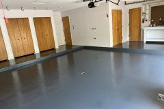 A garage interior with a smooth gray epoxy floor, several light wood doors, white walls, and a white workspace.