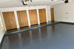 An empty garage with a smooth, glossy dark gray floor, white walls, and four wooden storage cabinets along the back wall.