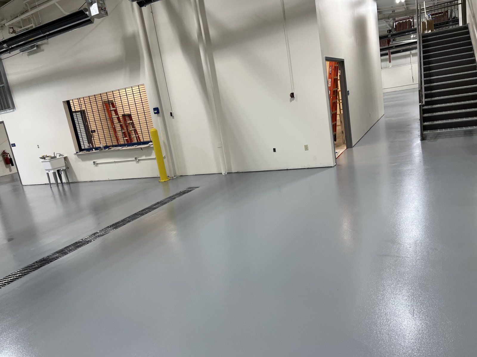 A view of a modern industrial indoor space with polished grey floors, white walls, a black metal staircase, and artwork.