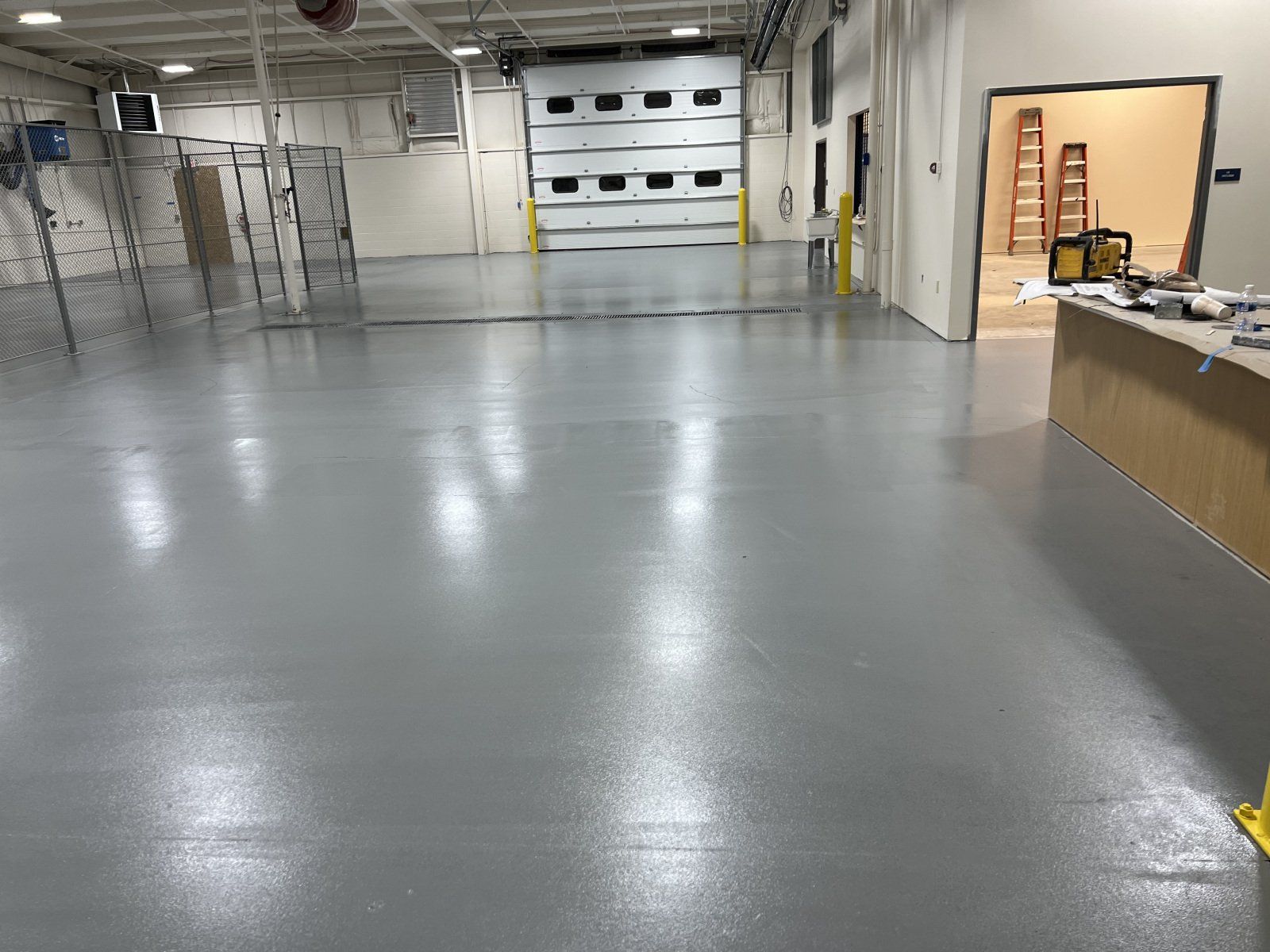 A large, open warehouse featuring a smooth, light grey epoxy floor and a closed overhead loading dock door.