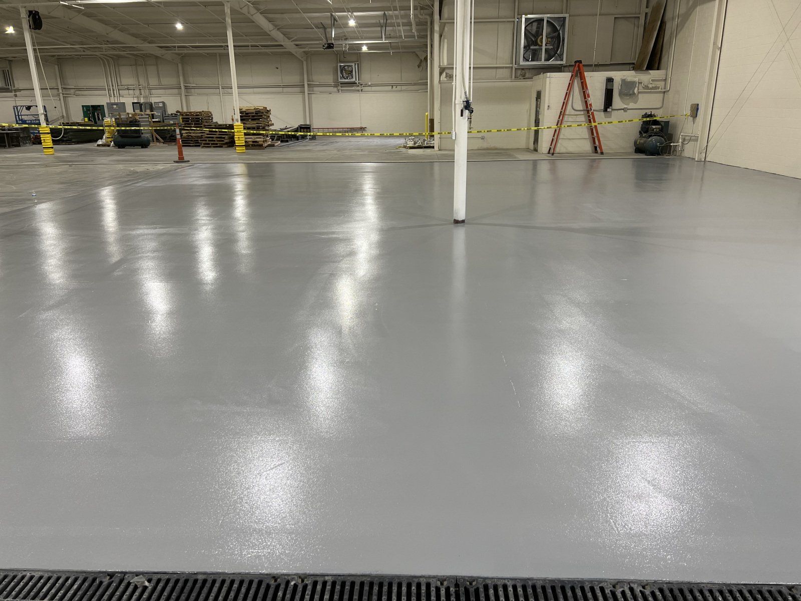 A freshly coated, glossy gray warehouse floor with overhead lights reflecting on the smooth surface.