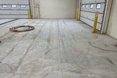 A concrete industrial garage floor with marked parallel lines and two garage doors with yellow safety bollards.