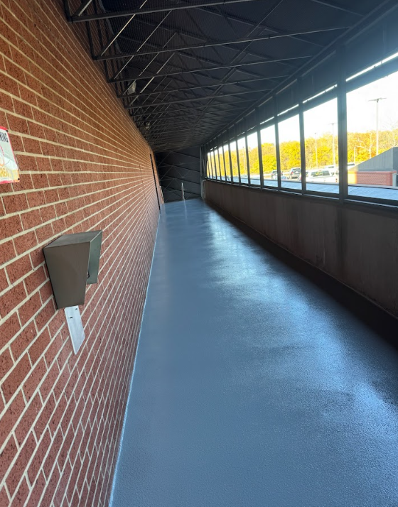 Empty covered walkway with brick wall, blue floor, and large windows along the right side.