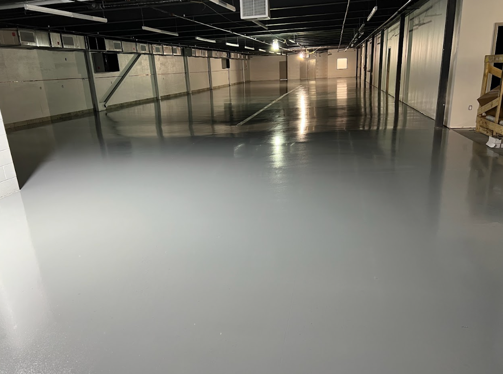 Empty warehouse interior with a glossy gray floor and overhead lighting lanes.