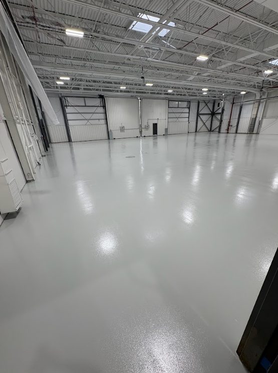 Empty white industrial warehouse interior with glossy floor and overhead lights.
