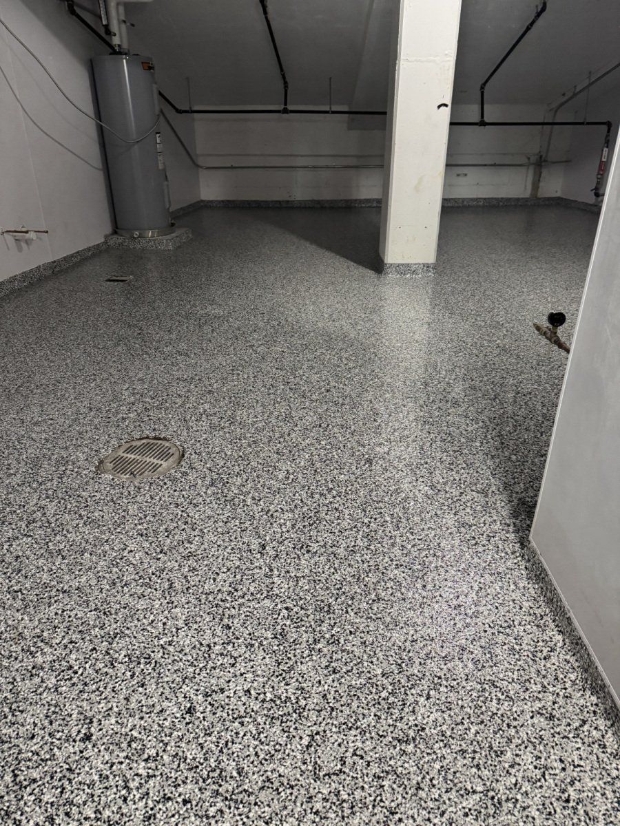 A basement room with a gray and white speckled epoxy floor, a water heater in the corner, and a central support pillar.