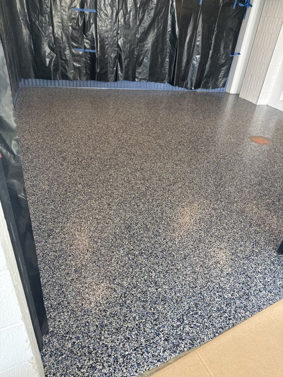 A finished garage floor featuring a grey, black, and white speckled epoxy coating with a high-gloss, reflective finish.