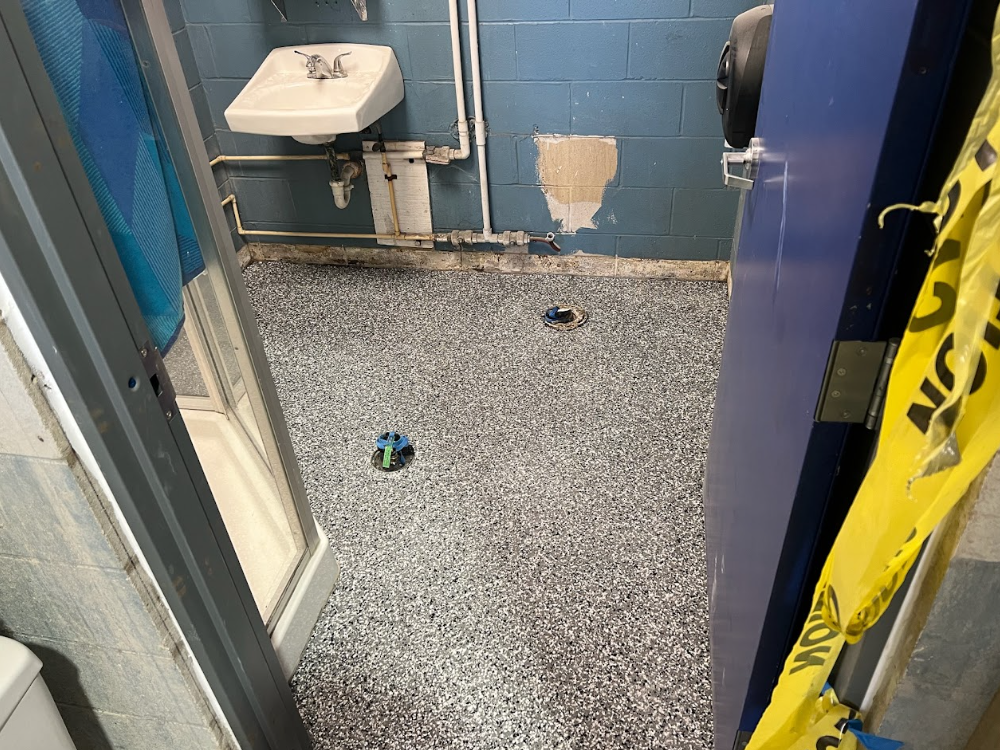 Public restroom with blue walls, a sink, a soap dispenser, and a speckled floor, viewed through a doorway.