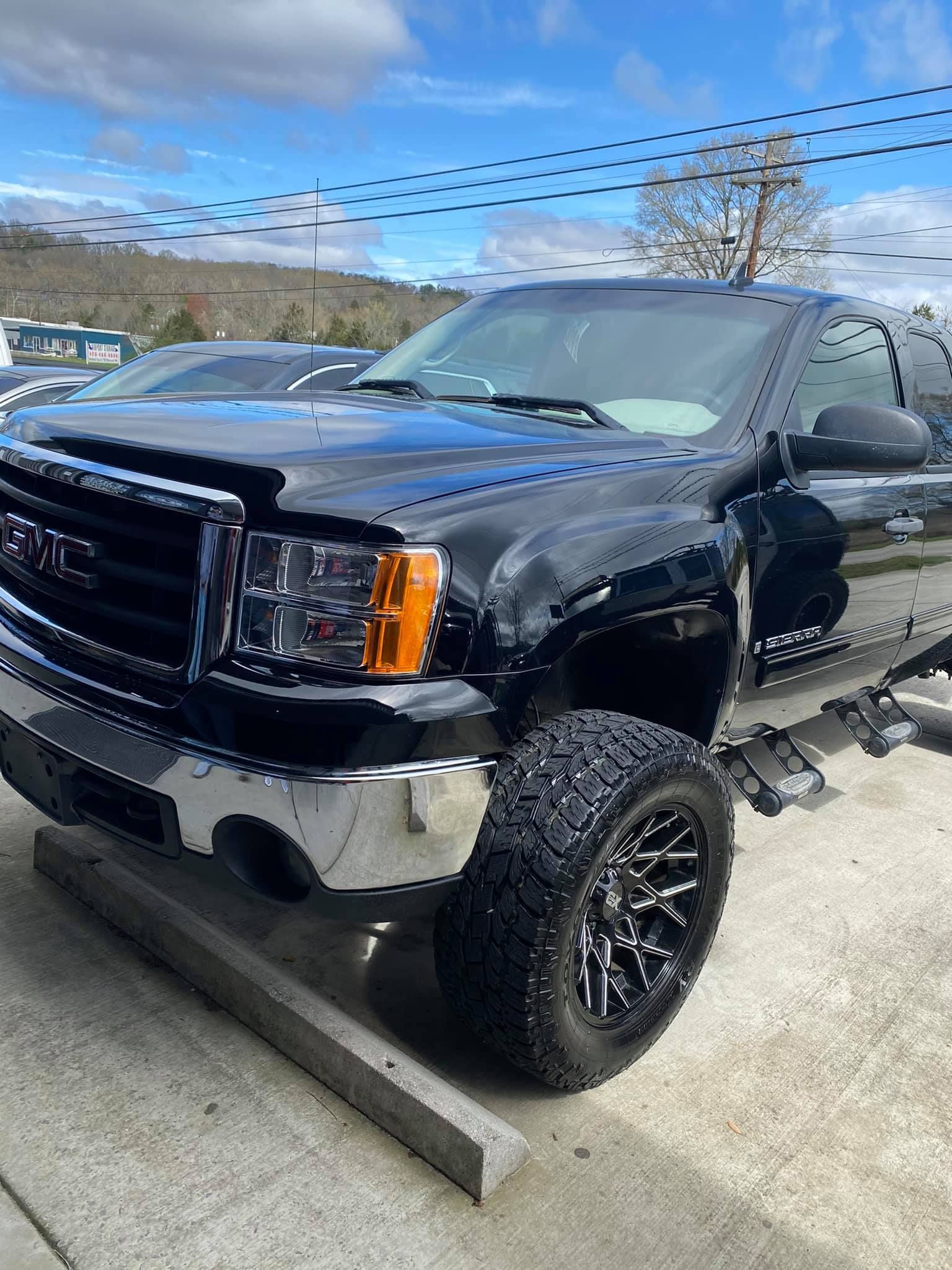 A black truck is parked on a curb in a parking lot.