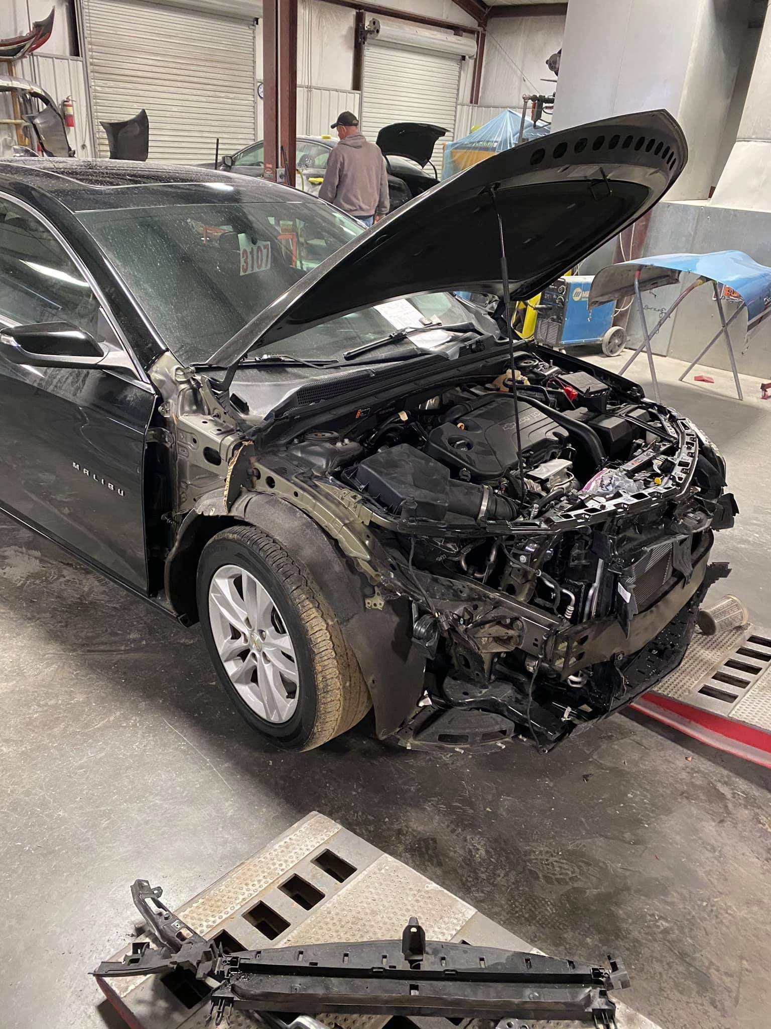 A black car with the hood open is sitting in a garage.