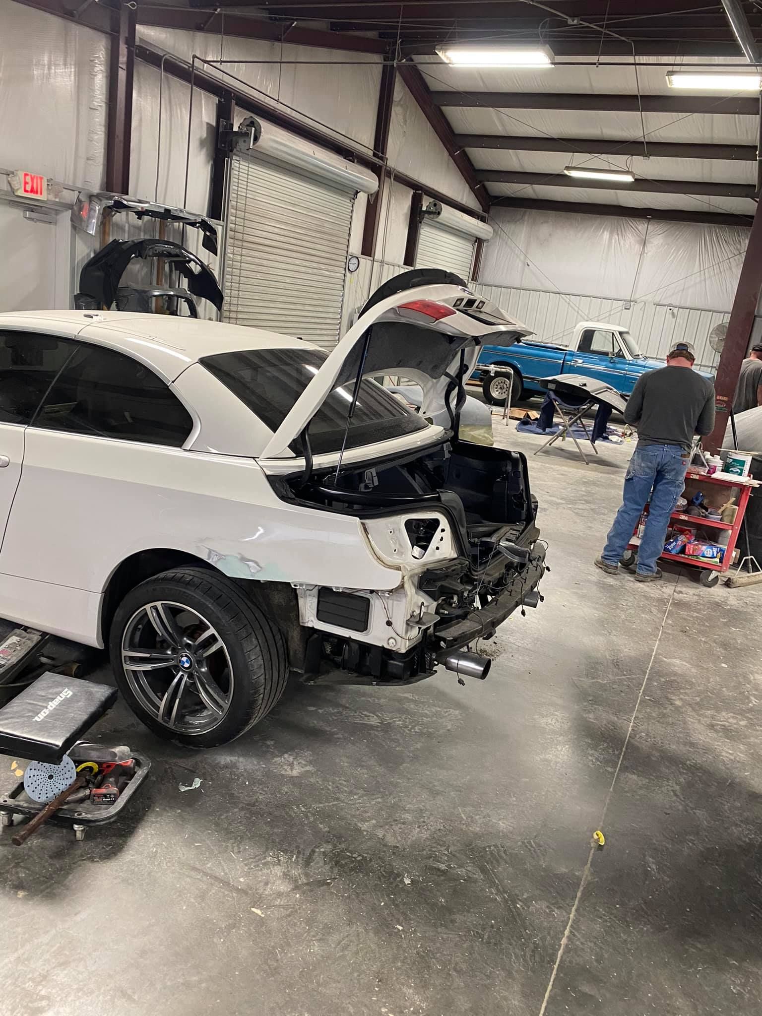 A white car is being repaired in a garage with the hood open.
