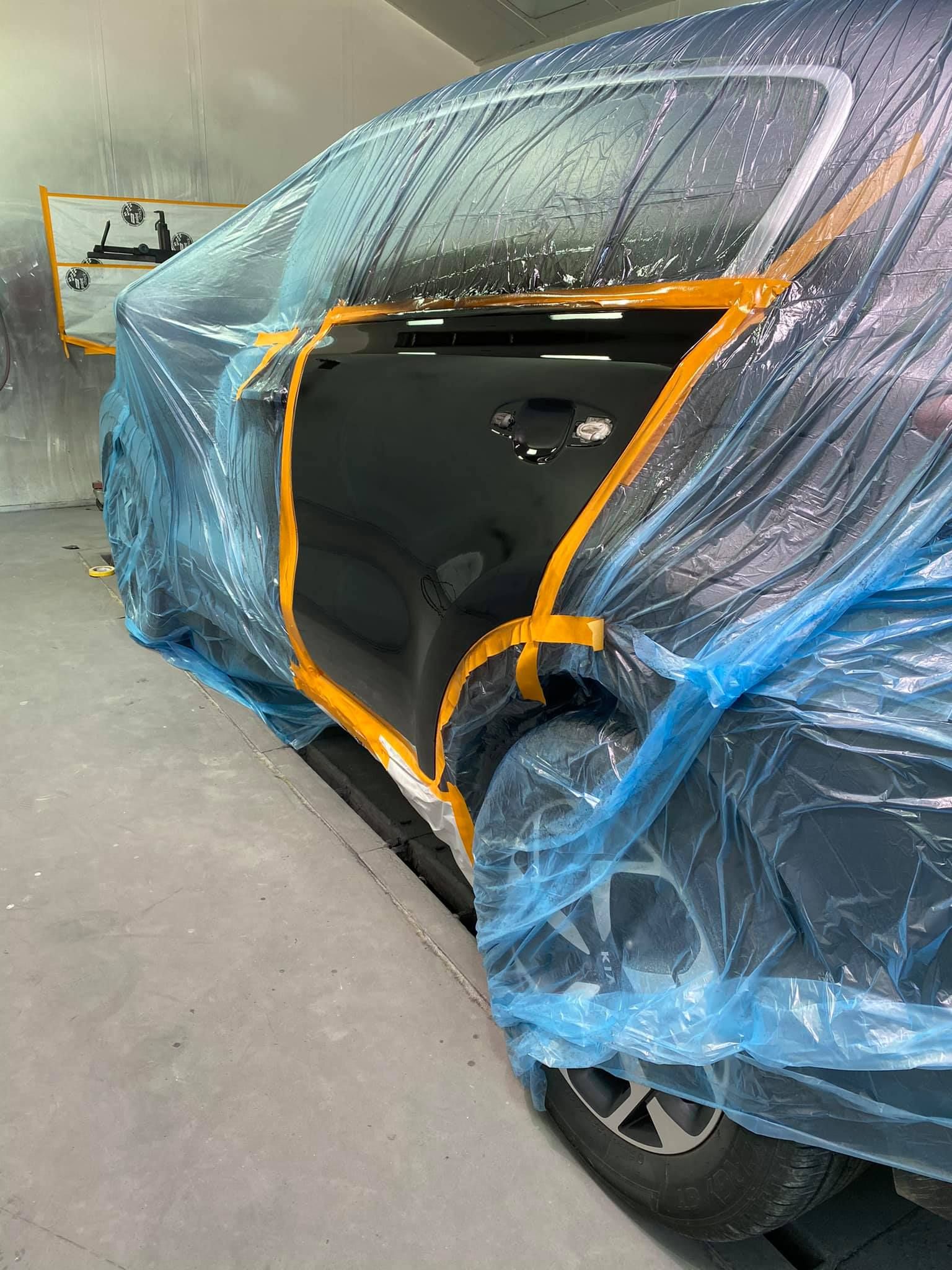 A car is wrapped in plastic while being painted in a garage.