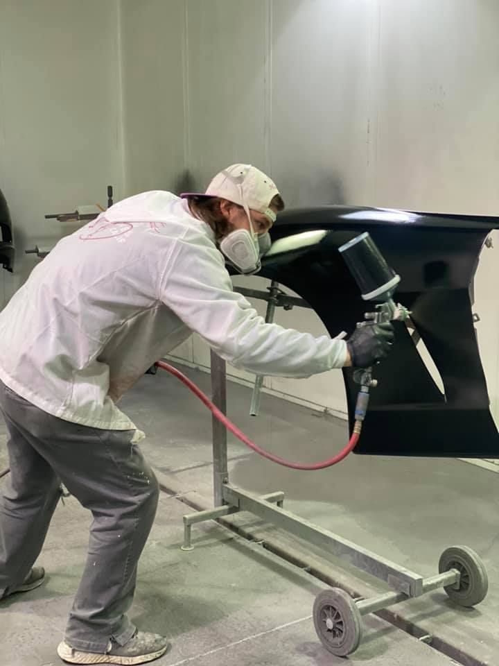 A man is spray painting a car in a paint booth.