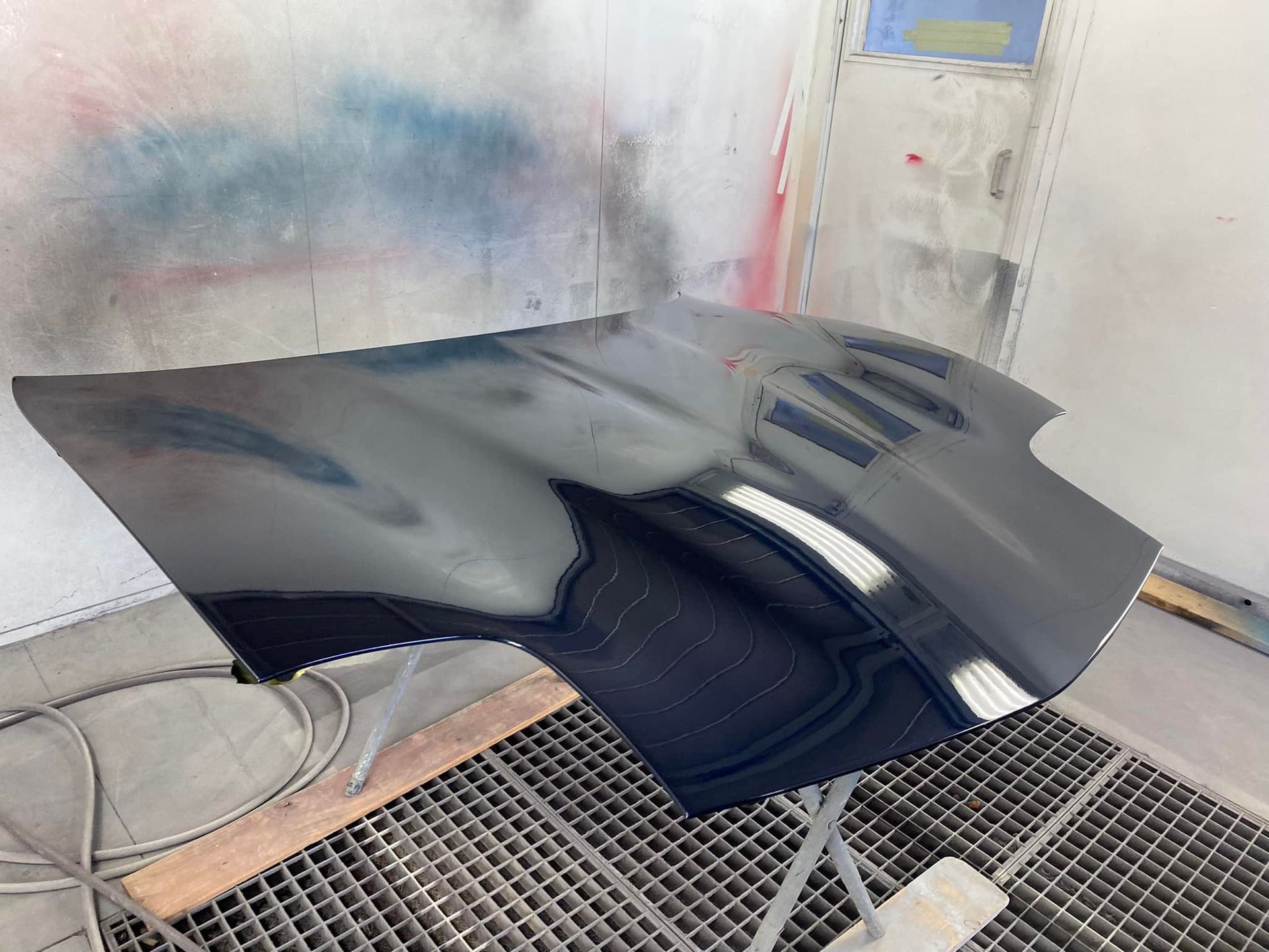 A black car hood is sitting on top of a metal grate.