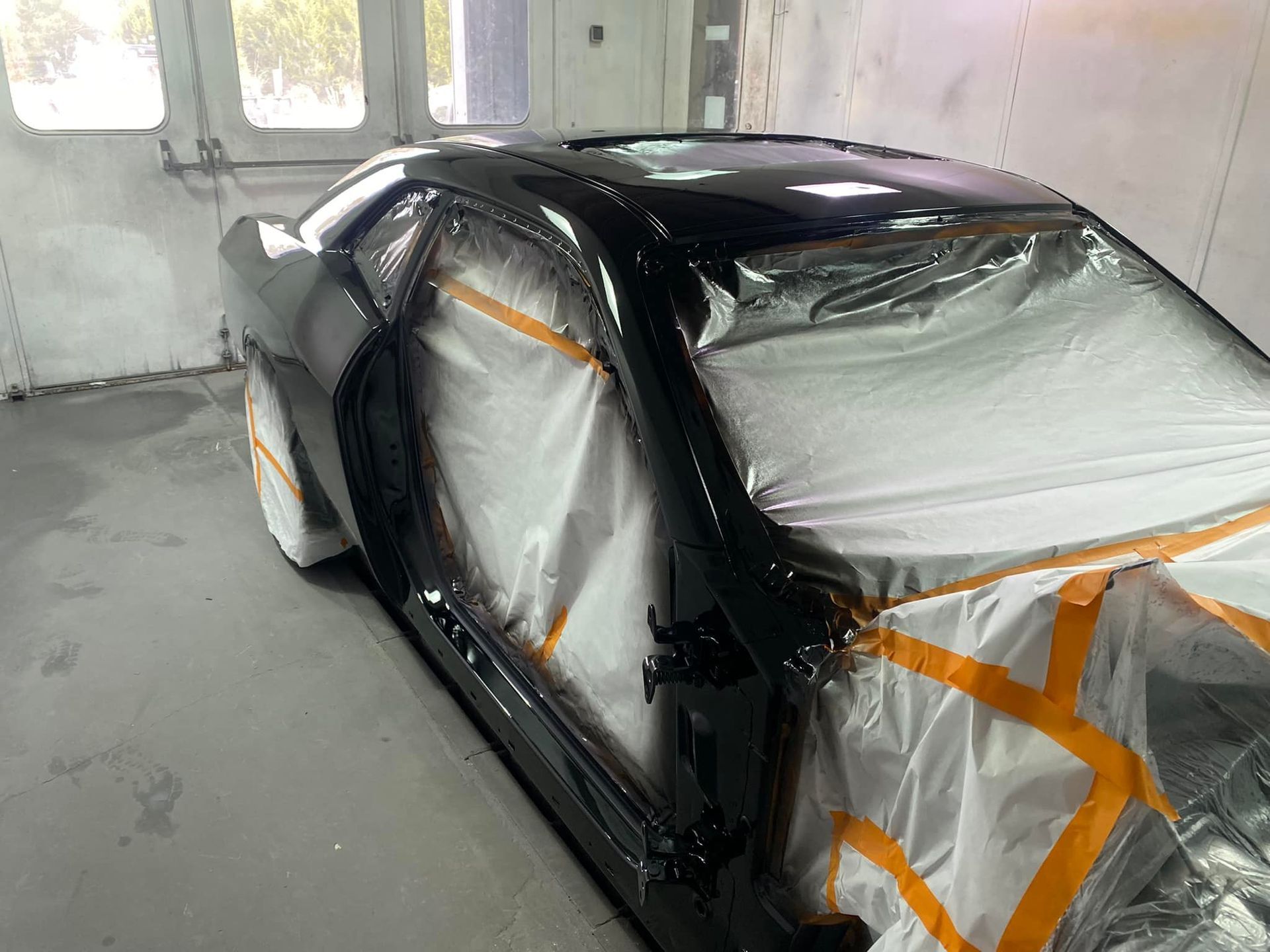 A black car is being painted in a garage.