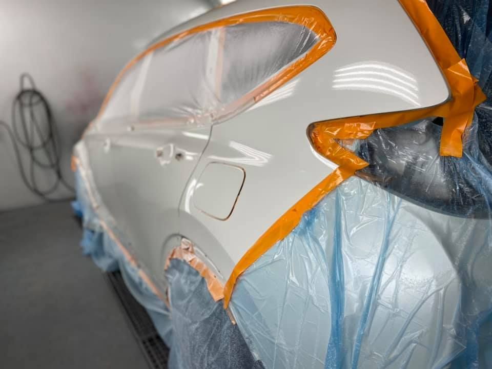 A white car is being painted in a paint booth.