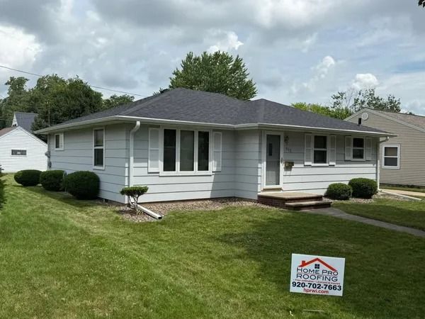 A light gray, single-story house with a new dark gray roof and a lawn sign for Home Pro Roofing in the front yard.