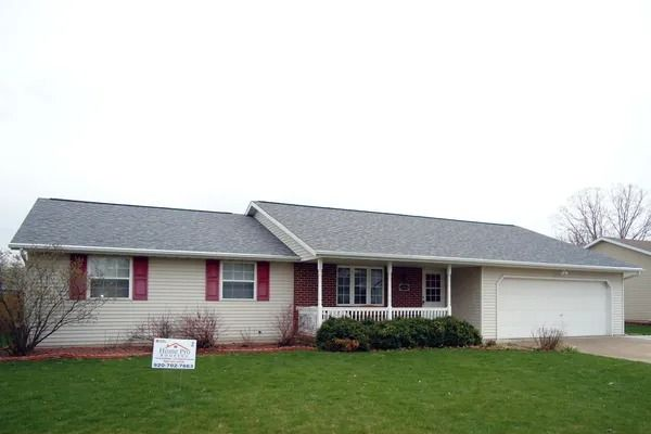 A single-story, beige ranch-style house with red shutters, a gray shingled roof, and an attached two-car garage.