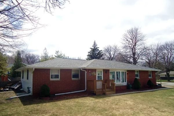 A single-story, red brick ranch-style house with a light gray roof and a wooden front porch on a grassy lawn.