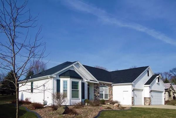 A single-story white house with dark shutters, a stone accent wall, and a multi-car garage under a clear blue sky.