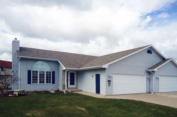 A light blue suburban house with a two-car garage and a front lawn under a cloudy sky.