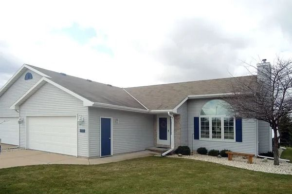 A light gray, single-story suburban house with a two-car garage, white trim, blue accents, and a large arched window.