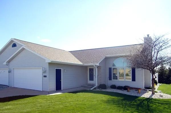 A one-story suburban house with light gray siding, a white garage door, a front door, and a large arched window.