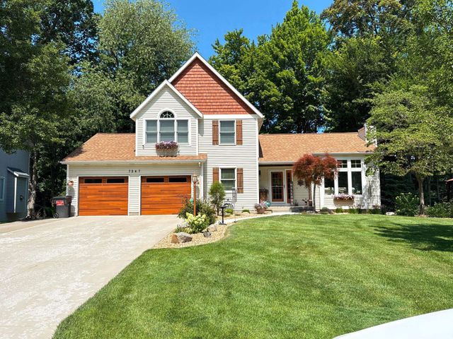 Two-story white house with orange trim, double garage, and a green lawn under trees.