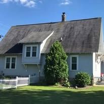 A light gray, two-story house with a steep, dark roof, white trim, and a white picket fence on a green lawn.