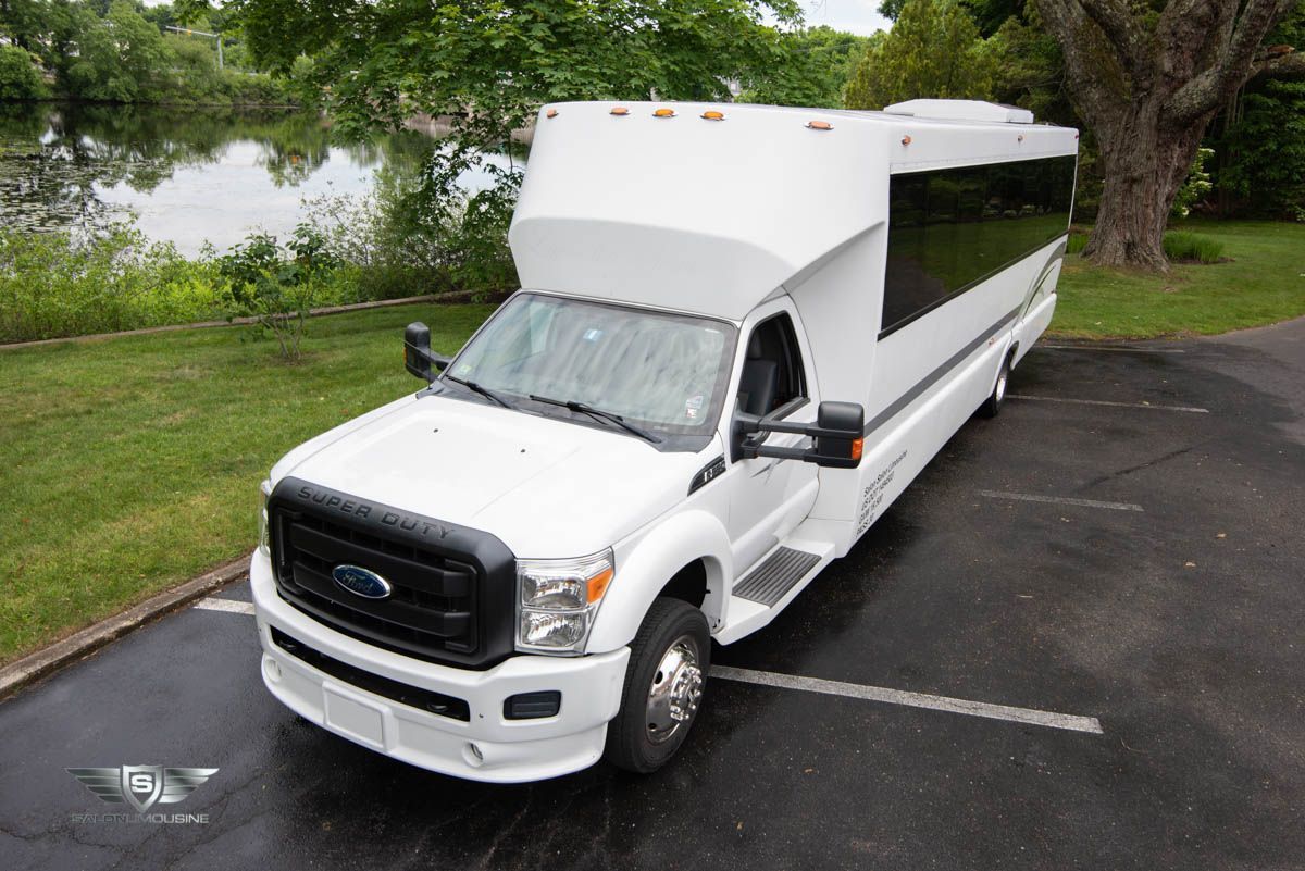 A white bus is parked in a parking lot next to a lake.
