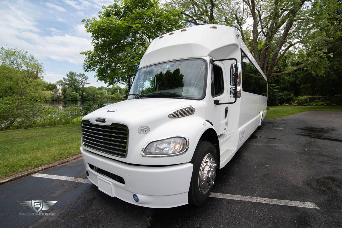 A white bus is parked in a parking lot with trees in the background.