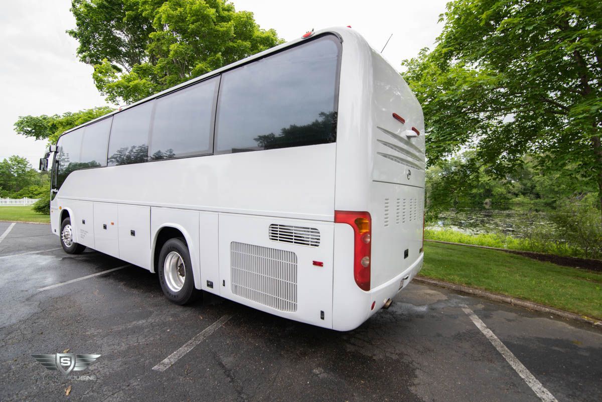 A white bus is parked in a parking lot with trees in the background.