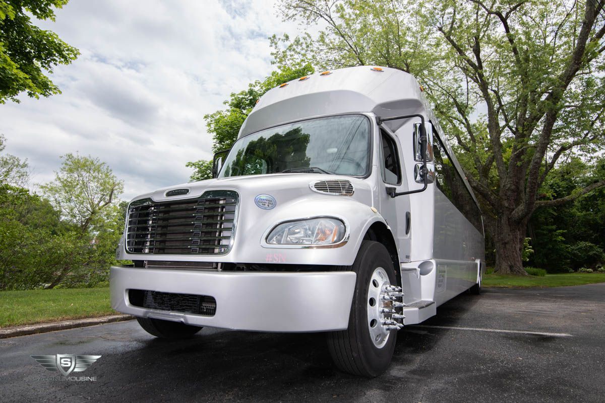 A white bus is parked in a parking lot with trees in the background.