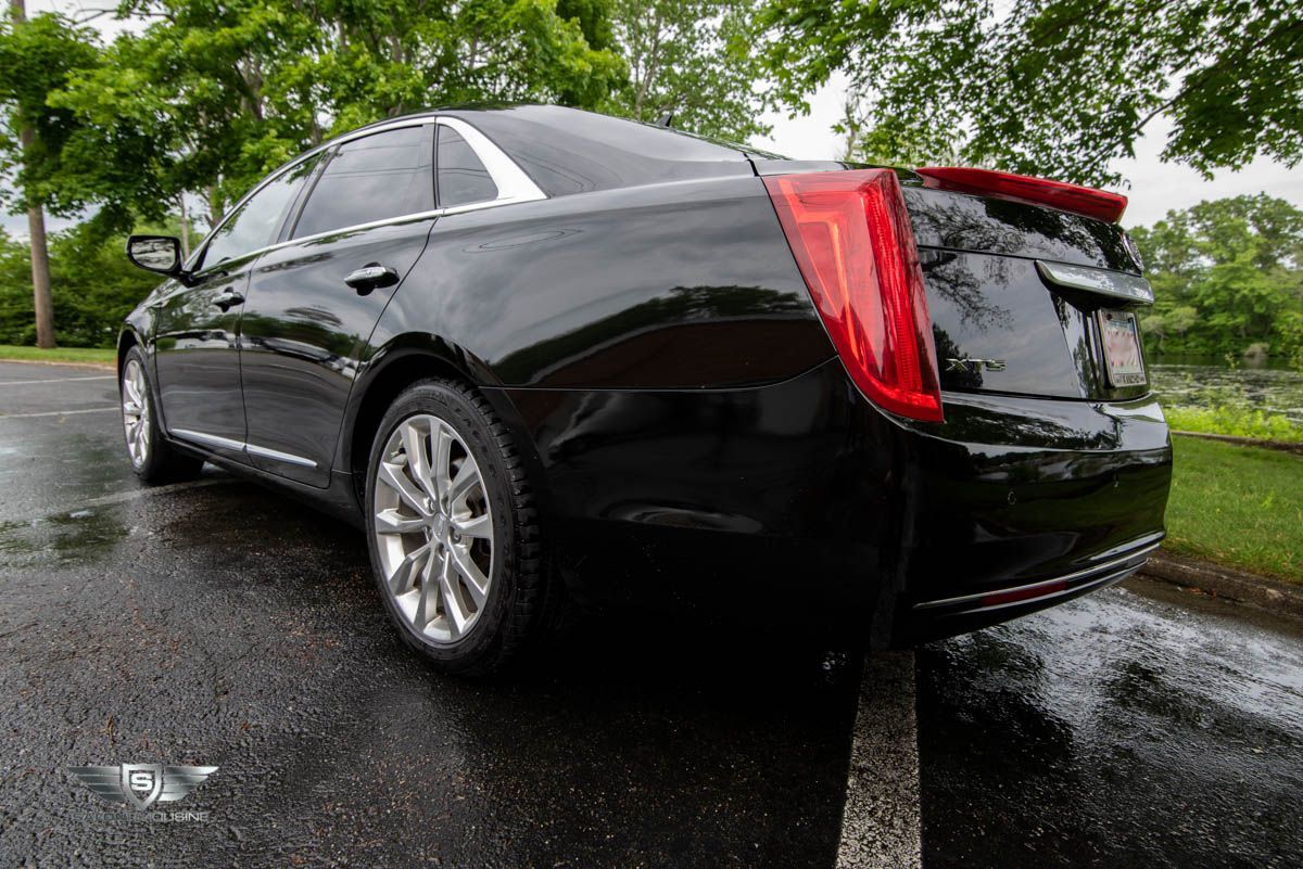 A black car is parked on the side of the road in the rain.