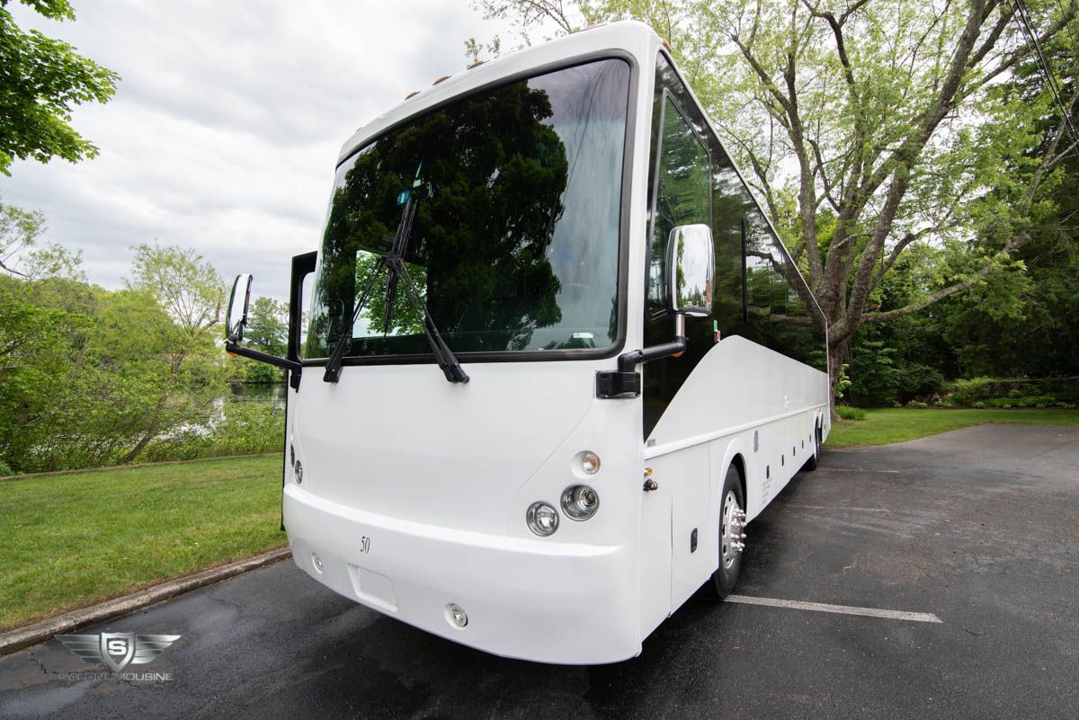 A white bus is parked in a parking lot with trees in the background.