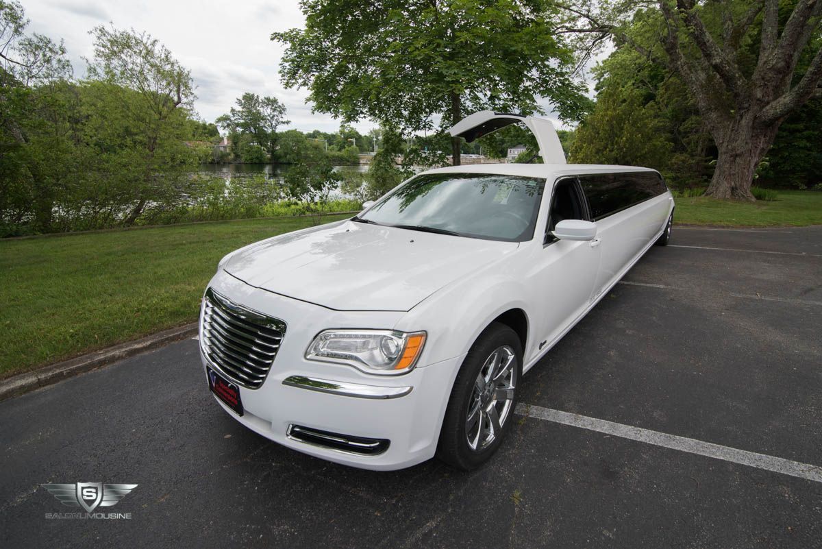 A white limousine is parked in a parking lot with its trunk open.