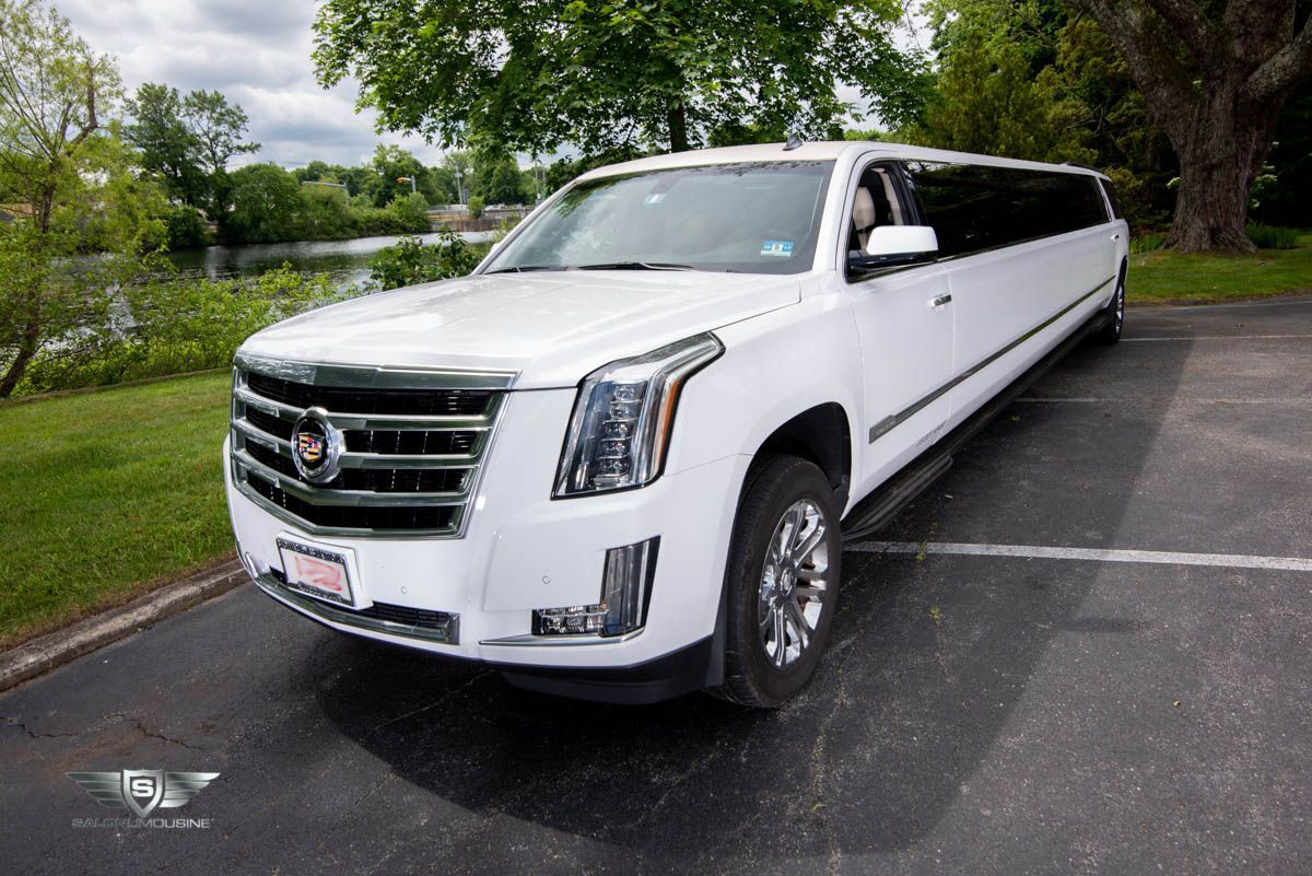 A white cadillac escalade limousine is parked in a parking lot.