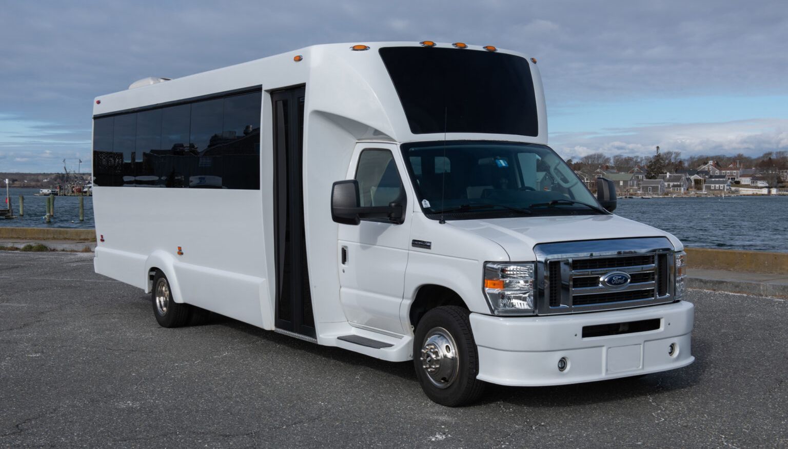 A white bus is parked in front of a body of water.