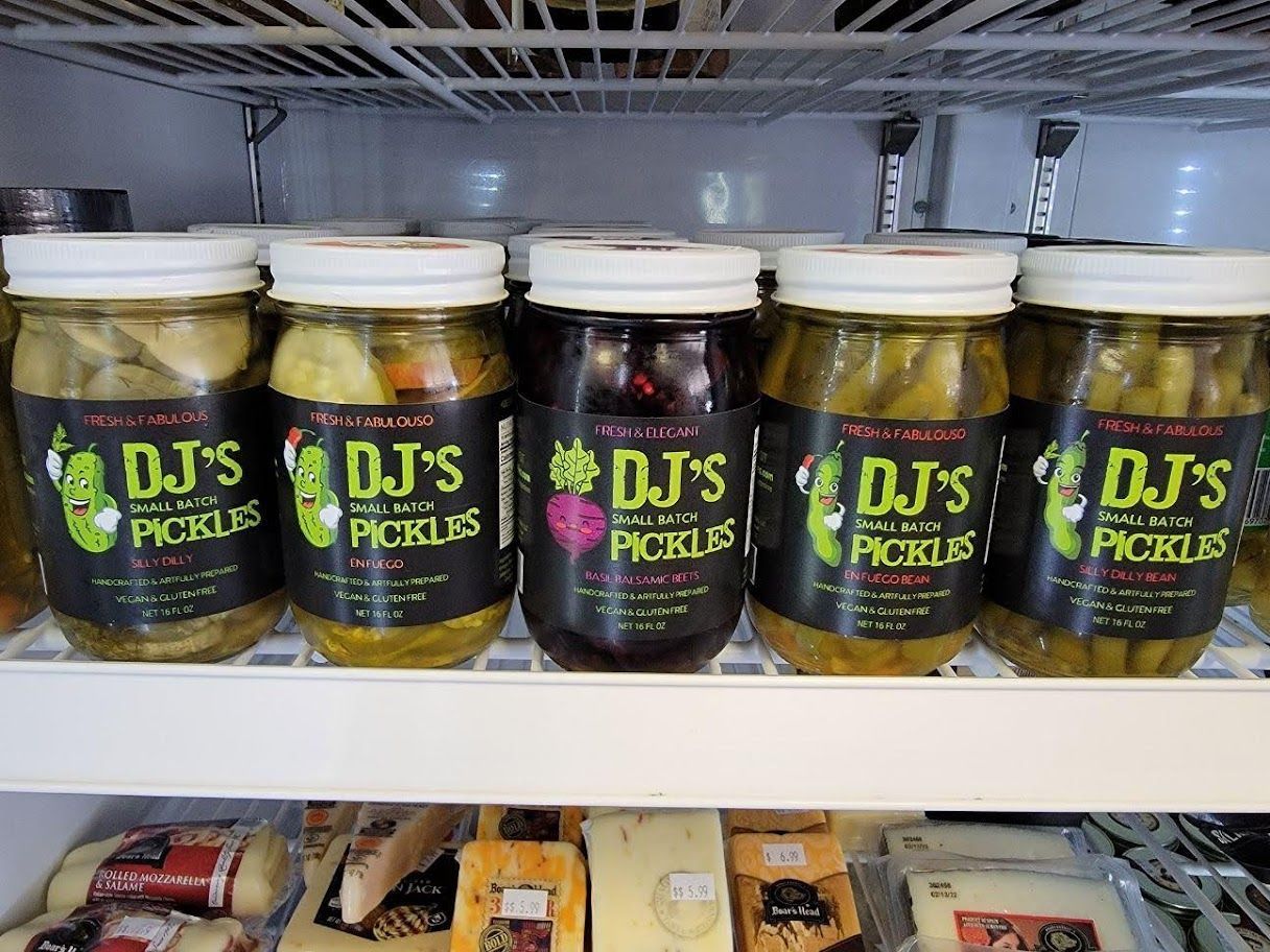 Jars of DJ's pickles in a refrigerated display case, featuring various colors and labels.