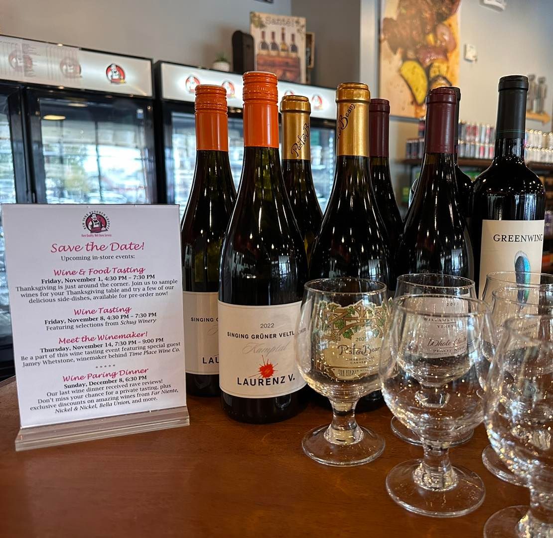 Wine bottles and glasses on a counter with a menu. Indoors, with a fridge in the background.