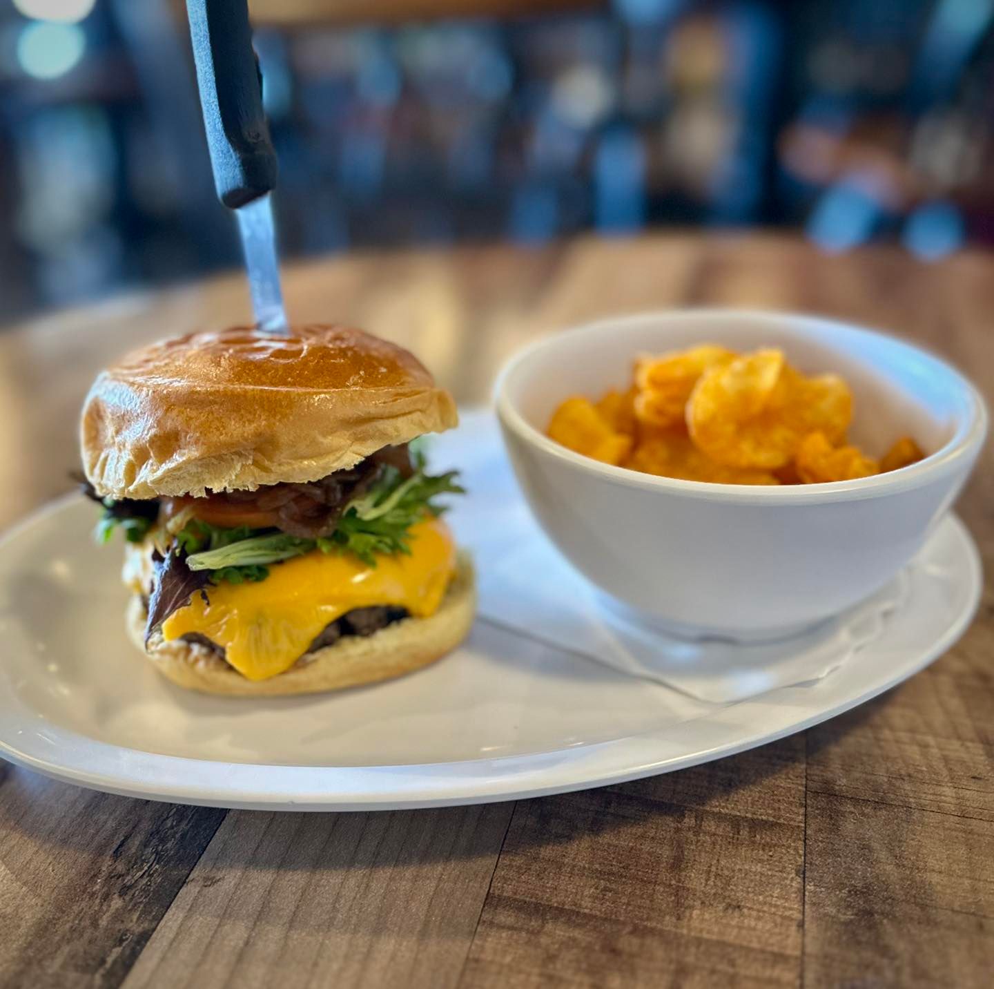 Burger with cheese and greens, served with a side of orange fried food, on a white plate.