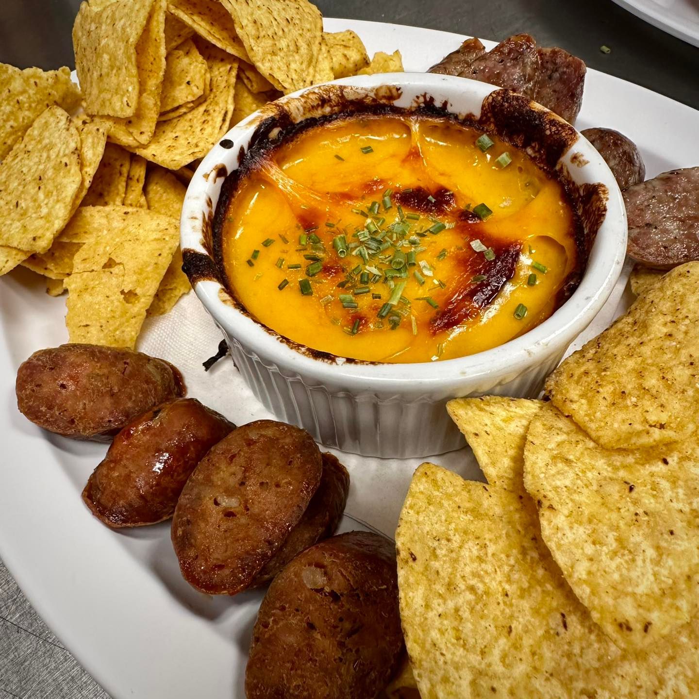 A plate with baked cheese dip, chips, and sausage bites.